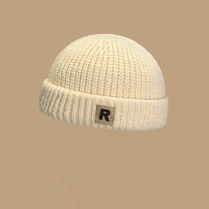 Detalle del gorro de punto acanalado blanco crema con parche de cuero marrón y la letra R