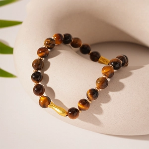 Detailed view of beaded tiger eye bracelet with gold fish charm on ceramic prop