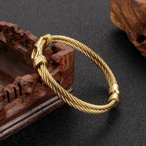 Detailed view of golden stainless steel braided wire rope bracelet on dark wood