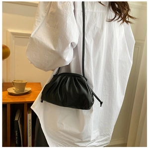 Detail of a black leather pleated cloud bag with a slim strap worn in a lifestyle setting
