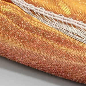 Macro shot of metallic gold knit fabric with white wavy lace and silver chain detail