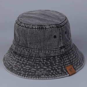 Detail of washed denim bucket hat featuring brown leather logo patch and metal eyelets