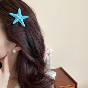 Detail of a light blue starfish hair clip with white pearl earring on a female model