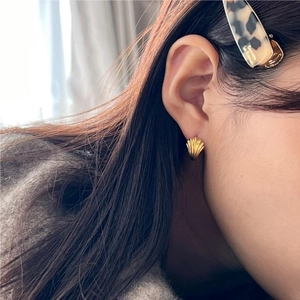 Detailed close-up of a model wearing small golden shell earrings with a textured matte finish