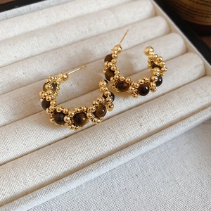 Detailed close-up of C-shaped hoop earrings featuring gold beads and tiger eye stones