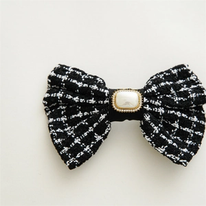 Macro detail of plaid tweed bow hair accessory with gold-rimmed pearl embellishment