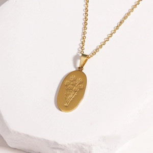 Detail of gold oval pendant necklace with floral engraving on white plaster