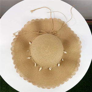 Detailed top view of a straw sun hat with shell decorations and wavy brim on a table