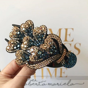 Close-up of a floral hair clip featuring navy blue rhinestones and gold accents held in hand