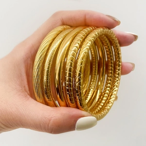 Set of gold titanium steel bangles with textured patterns shown on a model's hand
