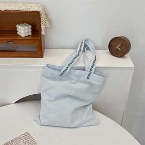 Détail du sac cabas en toile bleu clair montrant la broderie florale sur les anses