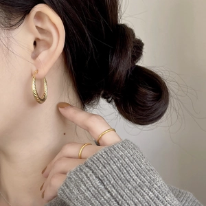 Close-up of elegant gold twisted hoop earrings and minimalist rings on a female model