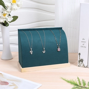 Dettaglio del supporto per collane in velluto verde scuro con base in legno in luce soffusa