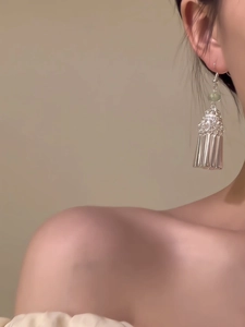 Détail de boucles d'oreilles argentées à pompons avec perles vertes portées sur modèle