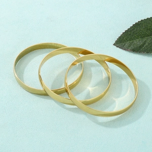 Three minimalist 8mm wide gold stainless steel bangles stacked on a light blue background