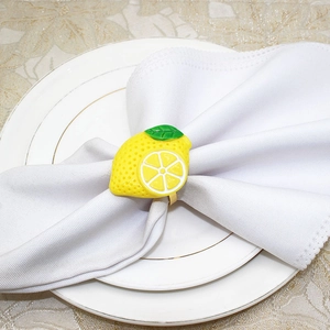 Close-up of yellow lemon slice napkin ring with green leaves on a white linen napkin