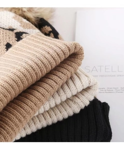 Detailed view of leopard print knit beanies with fluffy pom poms and ribbed folded edges