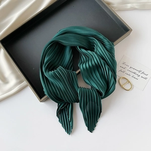 Detailed view of dark green pleated silk scarf texture on a minimal black tray display