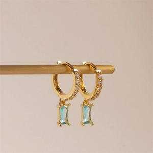Detail of gold huggie hoop earrings with rectangular light blue zircon drops and white stones