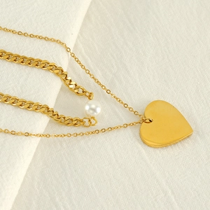 Double-layered gold necklace with heart pendant and pearl on white textured fabric