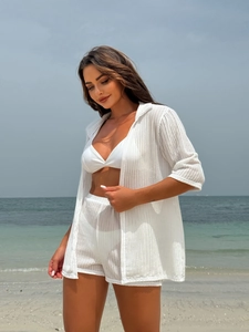 Close-up of white knitted beach set with bikini, shorts and mesh shirt in coastal setting