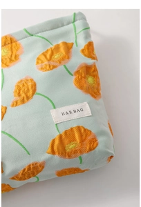 Close-up of canvas makeup bag with orange flowers and H&R BAG logo label texture