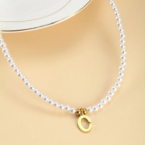 Detailed close-up of white pearls and golden metal C pendant on a necklace