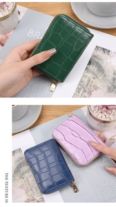 Three crocodile embossed leather mini wallets in green, blue and purple on a magazine