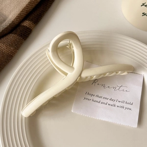 Grosse pince à cheveux crème mate sur une assiette texturée dans un décor minimaliste chic