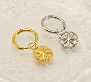 Detail view of gold and silver sunburst drop earrings with star relief on glass surface
