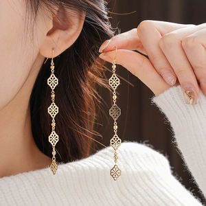 Close-up of golden geometric hollow dangle earrings worn by a model in a warm setting