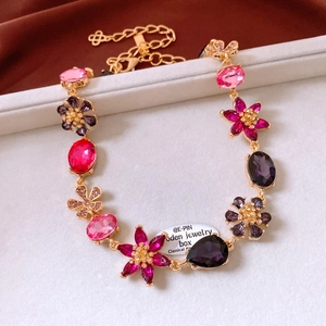Detail of vintage gold flower necklace with pink and purple gemstones on beige velvet