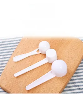 Set of three white plastic measuring spoons on a wooden board with blue striped fabric