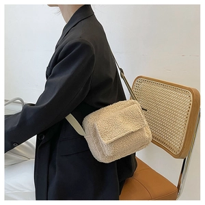 Detail of beige fleece crossbody bag with adjustable strap worn by model in a room