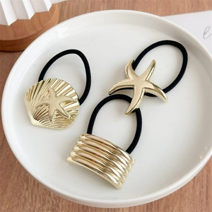 Close-up of gold starfish and shell charms on elastic hair ties in a white ceramic plate