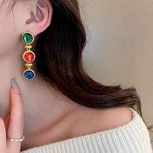 Détail de boucles d'oreilles vintage avec pierres vertes rouges et bleues sur modèle