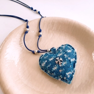 Gros plan détaillé du pendentif cœur en denim bleu avec croix en argent sur plateau