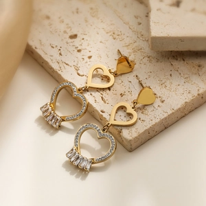Elegant gold heart earrings with zircon crystals on natural stone and fabric background