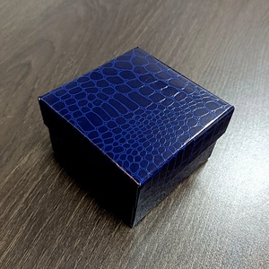 Detail view of square navy blue crocodile texture jewelry gift box on dark wood surface