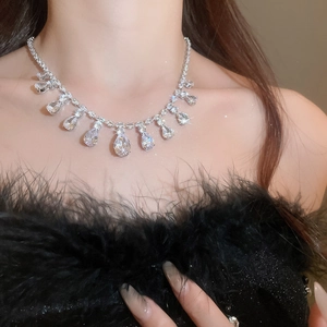 Detailed view of luxury zircon teardrop fringe necklace on a model with elegant black feathers