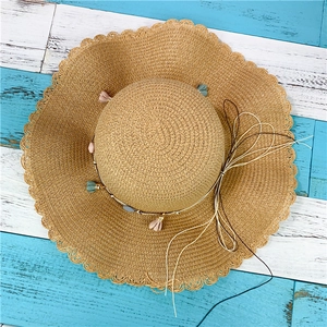 Detail of wide brim straw hat featuring scalloped edges and colorful tassel decorations