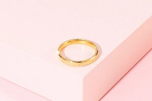 Detail of matte gold stainless steel ring with diagonal grooves on pink display stand