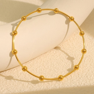 Minimalist gold stainless steel beaded bangle bracelet on white textured surface