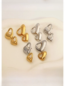 Detailed flat lay of hollow heart drop earrings in gold and silver steel on ceramic tray