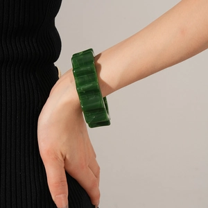 Detail of a deep green acrylic wide bangle with wavy textured pattern on woman's wrist