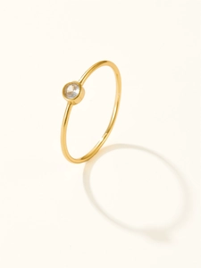Detail of minimalist gold plated silver ring featuring a single clear zircon on a cream base