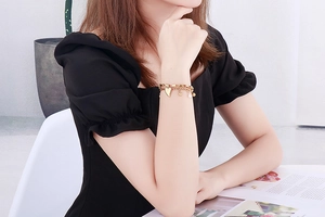 Détail d'un bracelet doré multicouche avec breloque cœur, billes et perle blanche au poignet