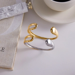 Polished gold and two-tone stainless steel open cuff bangles set on a white table