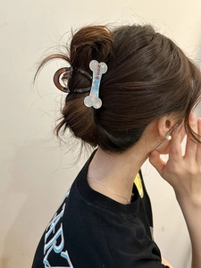 Close-up of a pearlescent bone-shaped hair claw clip on a model's hair bun