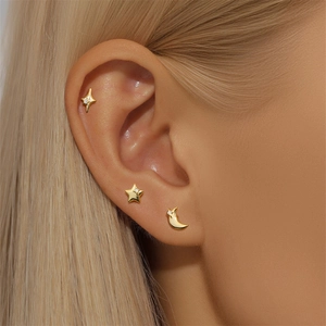 Close-up of gold clover star and moon stud earrings with zircon stones on ear